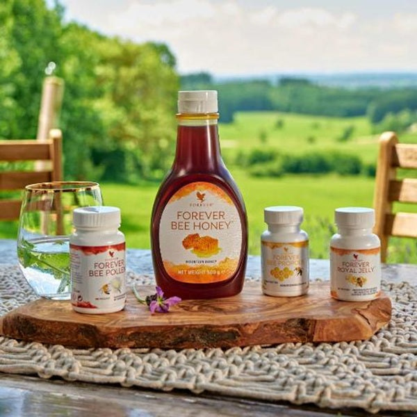Bottle of Forever Bee Honey with smaller bottles on a wooden board outdoors.