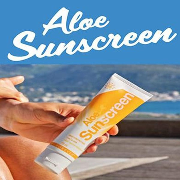 Person holding a tube of aloe sunscreen with a beach background