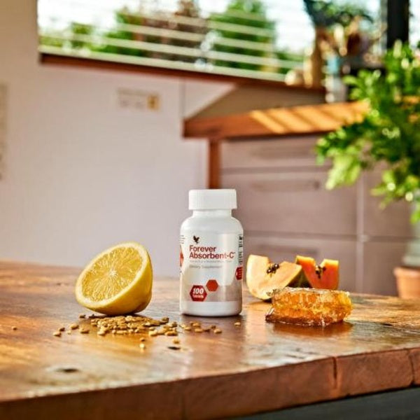 Supplement bottle labeled 'Forever Absorbent-C' on a wooden table with fruits and seeds.