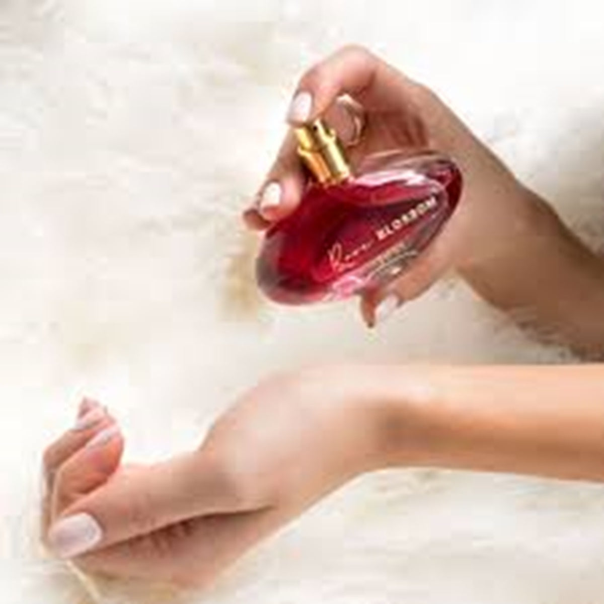 Hand holding a red perfume bottle with a gold cap on a light background